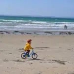 How to Teach Bike - child riding a bike on the wet sand of the beach